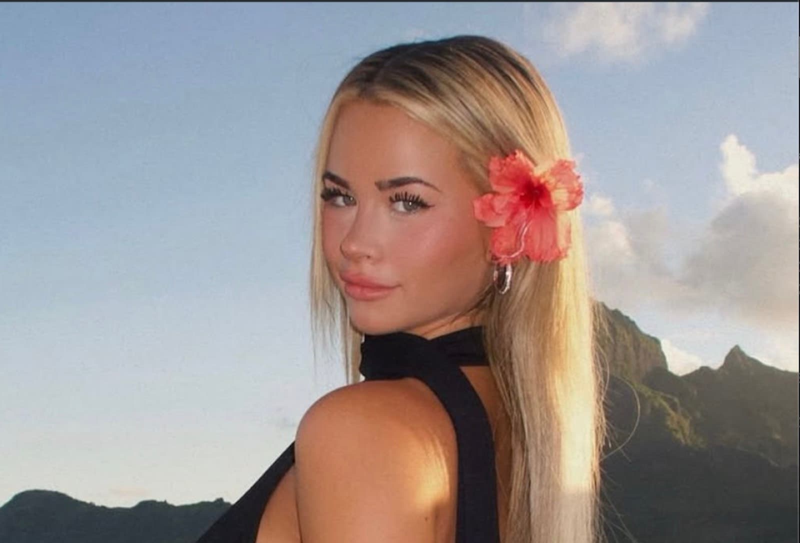 Emily looking over her shoulder, a red hibiscus in her hair, mountains behind